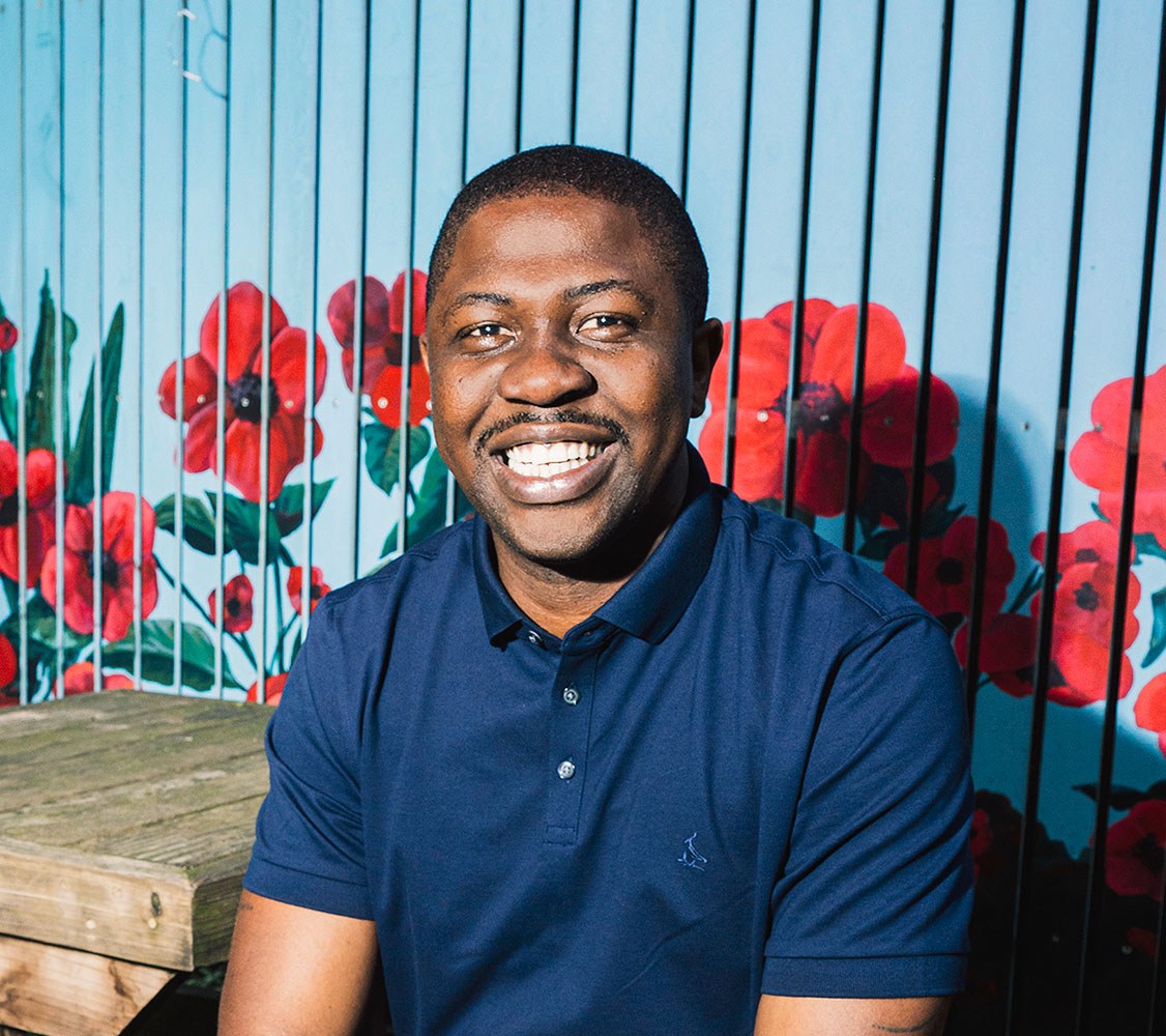 Portrait of Edafe Okporo smiling in front of a wall with red flower illustrations