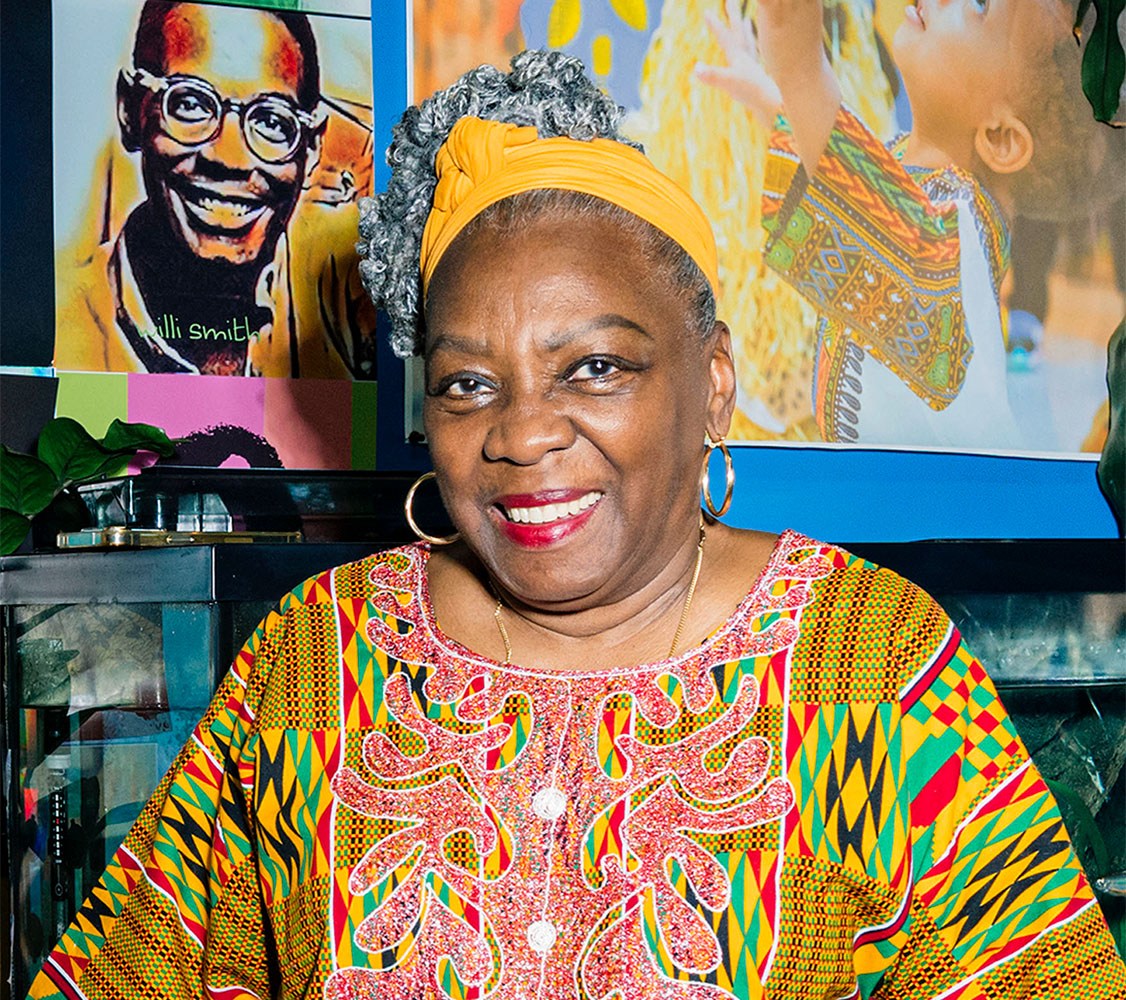 Portrait of Fela Barclift smiling in front of a wall with artwork