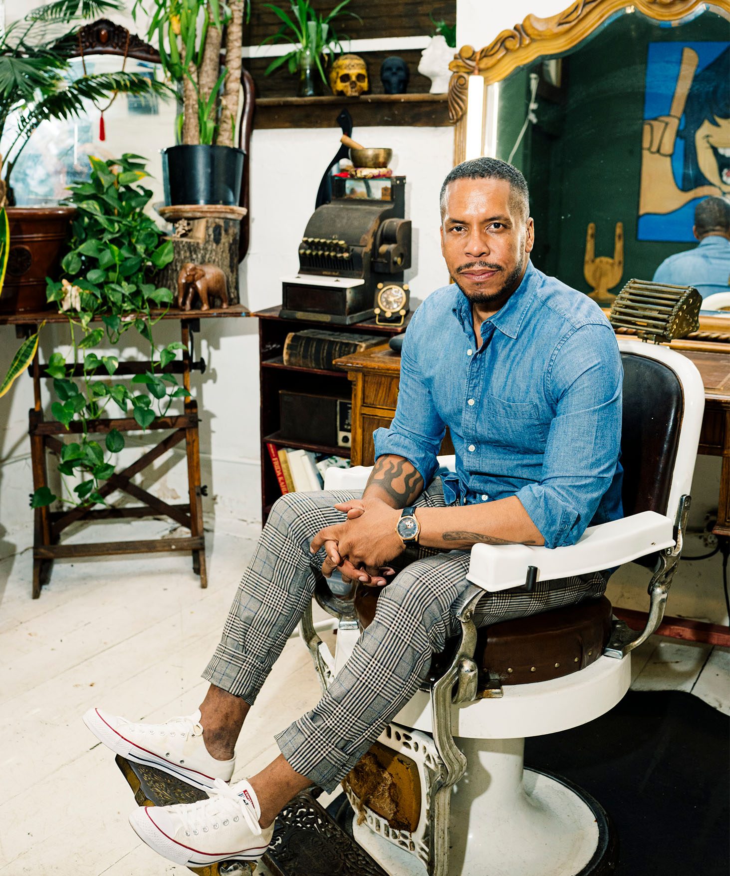Gregory Purnell seated on a barber's chair in his studio with plants in the background.