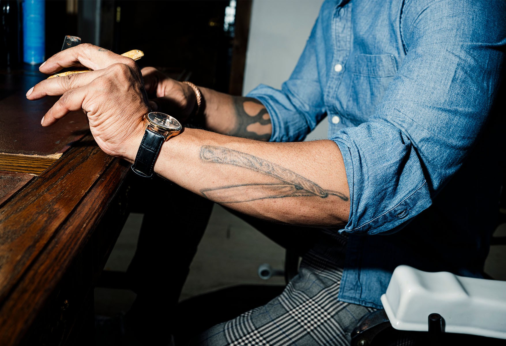 An arm with the shirt sleeve rolled up to reveal a barber's razor tattoo