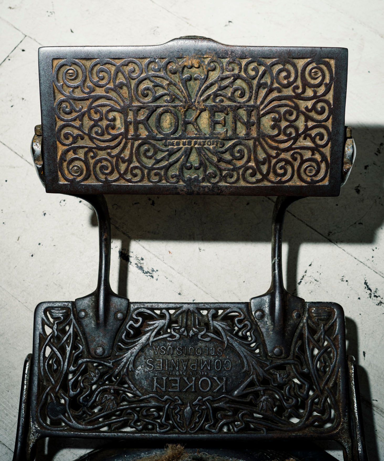 Top down view of a foot rest of an antique barbershop chair with the manufacturer name Koken surrounded by ornamental patterns, cast in iron.