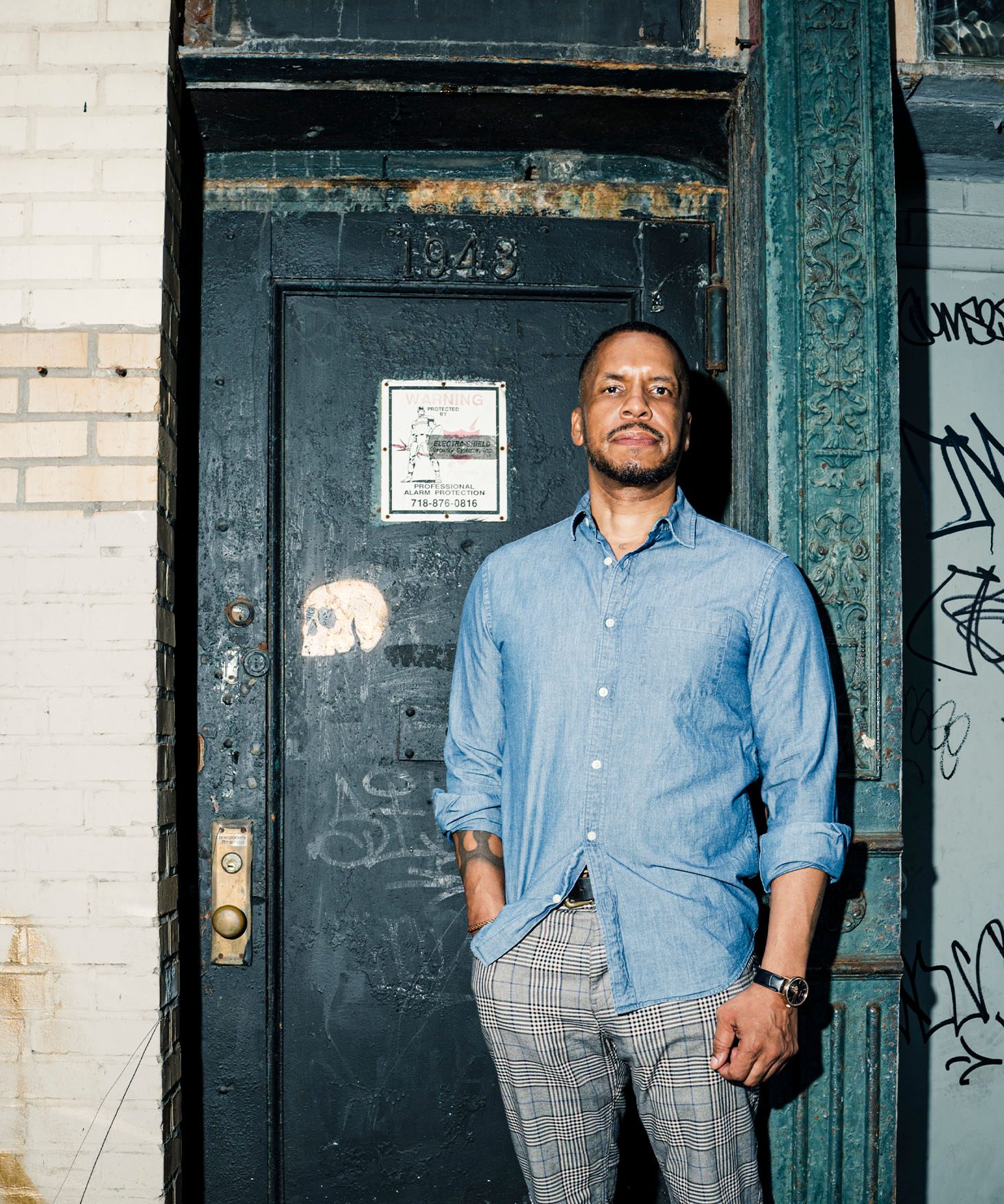 Gregory Purnell stands in front of the door of the building where his studio is located. A small stenciled image of a scull is painted on the door in metallic paint.