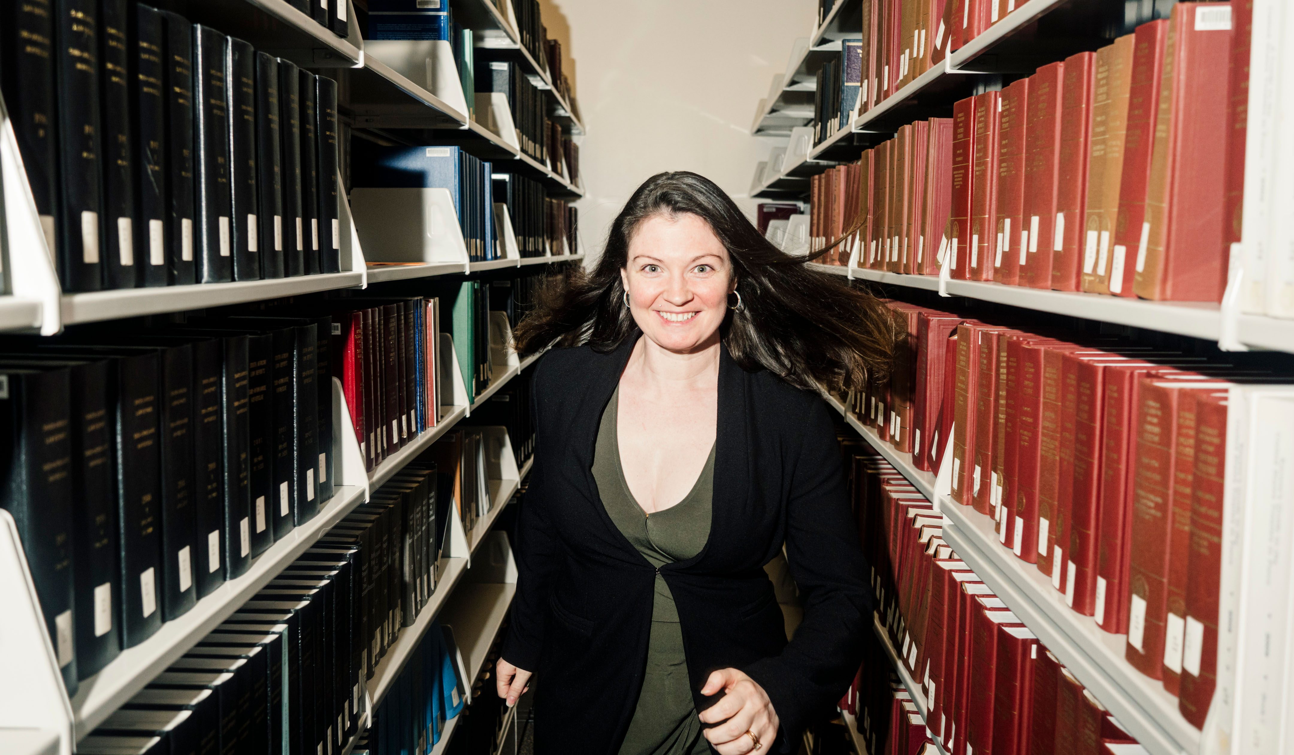 Christine DeMaria smiling, in a library aisle, running towards the camera.