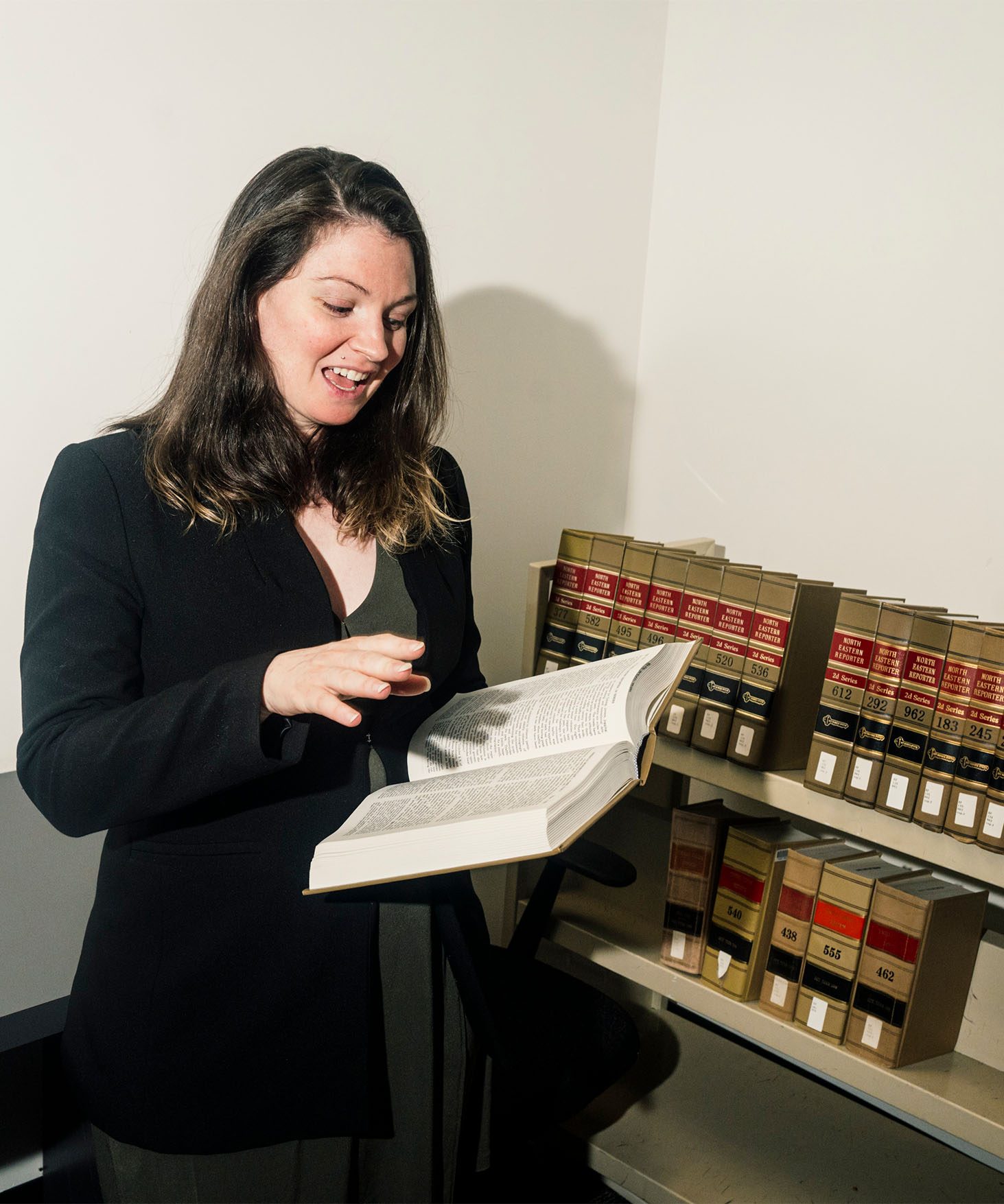 Christine DeMaria with an open law book, reading out loud. More law books are visible on shelves in the background.