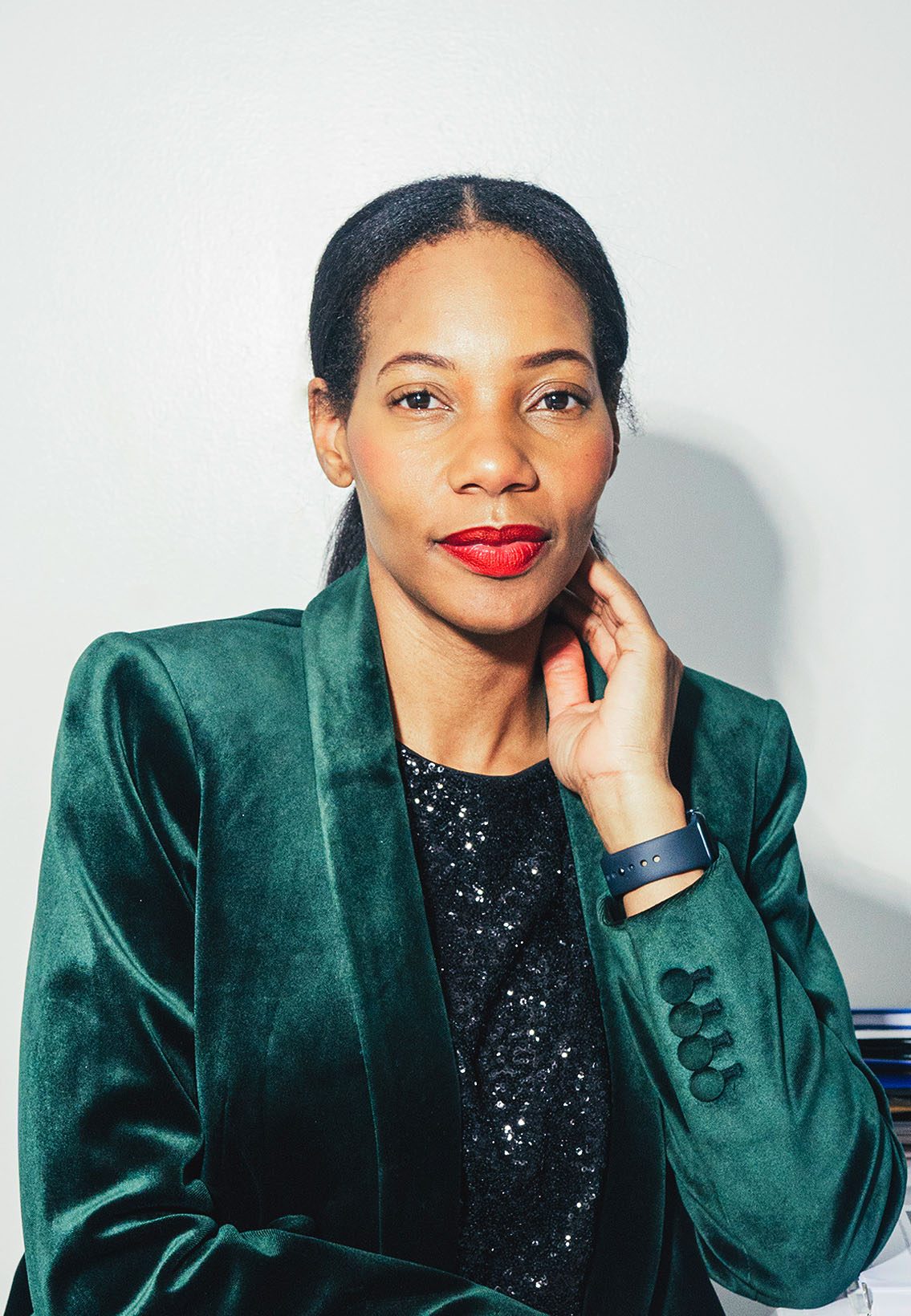Portrait of Dianna Rose in a black sequin top and green velvet blazer seated in front of a white wall.