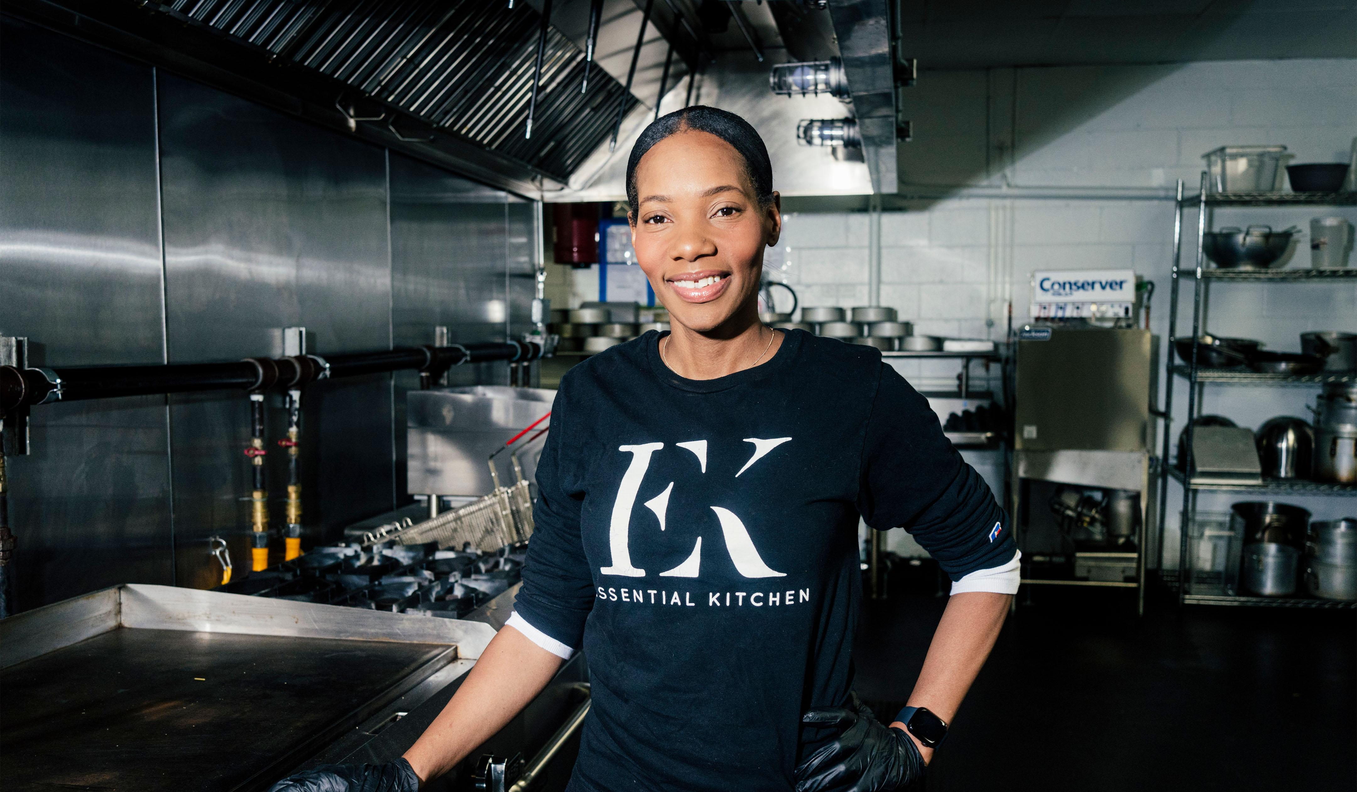 Dianna Rose, smiling in a commercial kitchen with stainless steel and tiled walls.