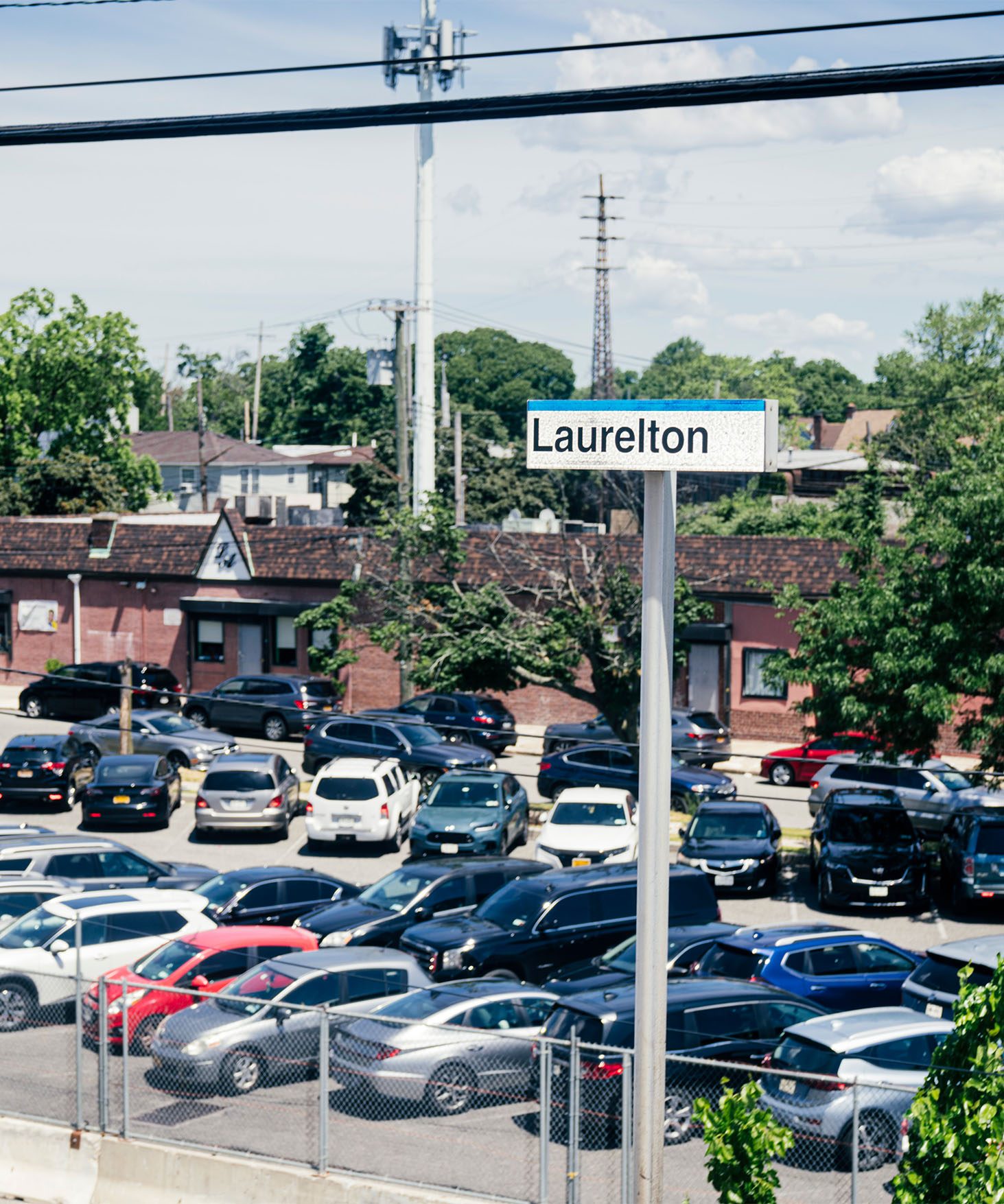 View of a parking lot full of cars at a LIRR train station. A sign reads “Laurelton.”