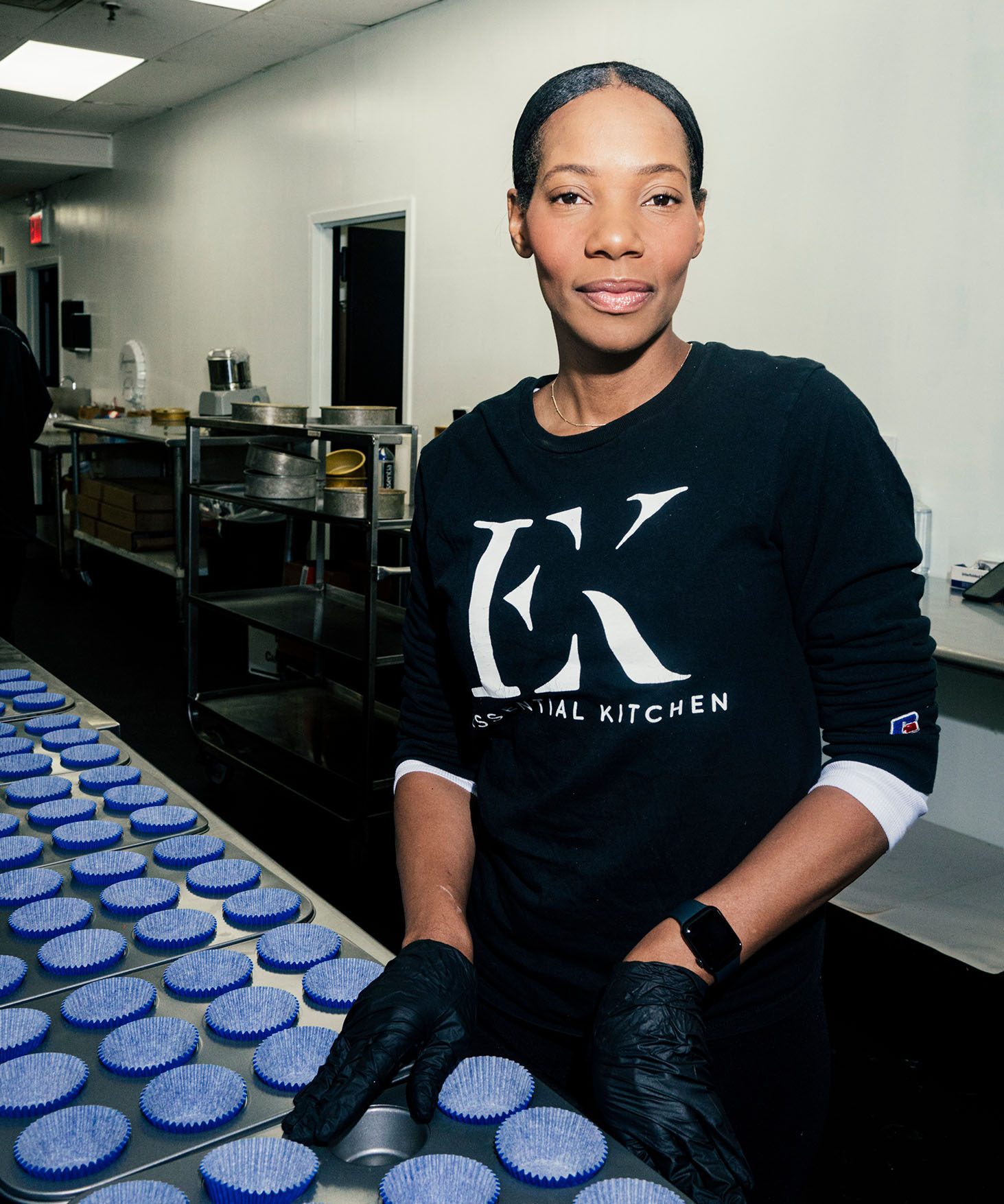 Dianna Rose working in a kitchen. In front of her is a table full of neatly organized baking trays with blue cupcake paper liners.