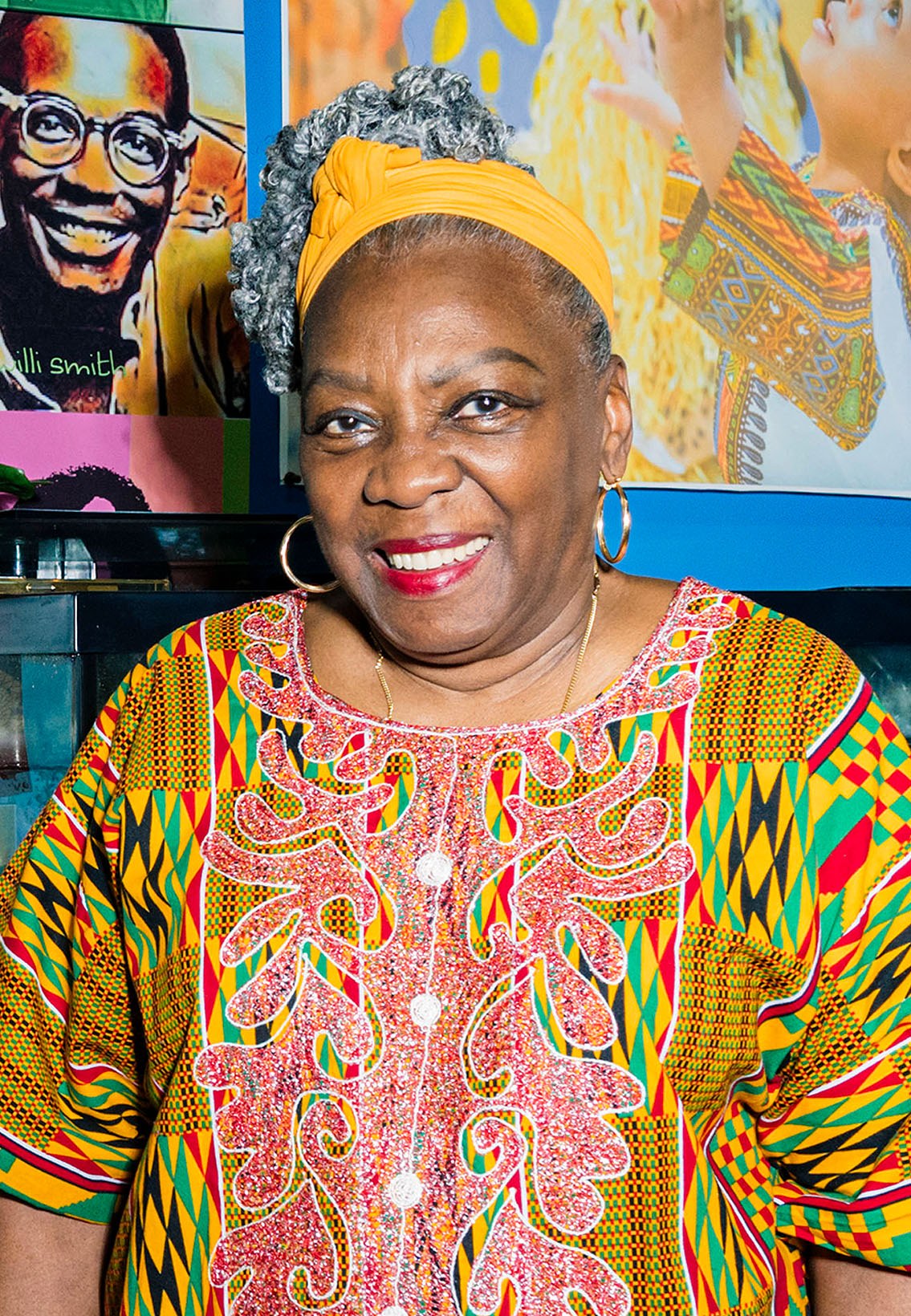Portrait of Fela Barclift smiling, in front of a blue wall with artwork.