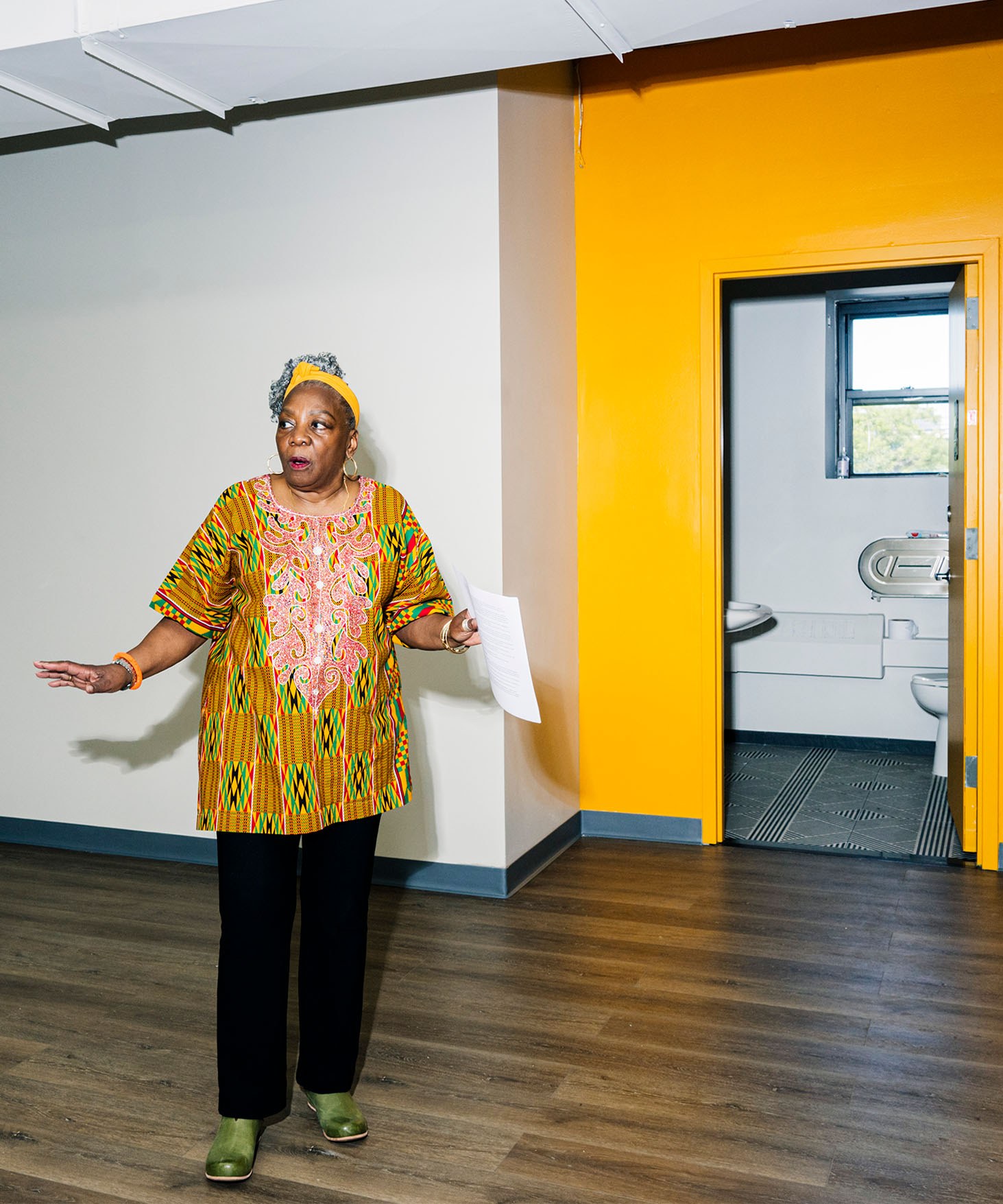 Fela Barclift standing in a classroom with a bright yellow wall in the background that complements her clothing.