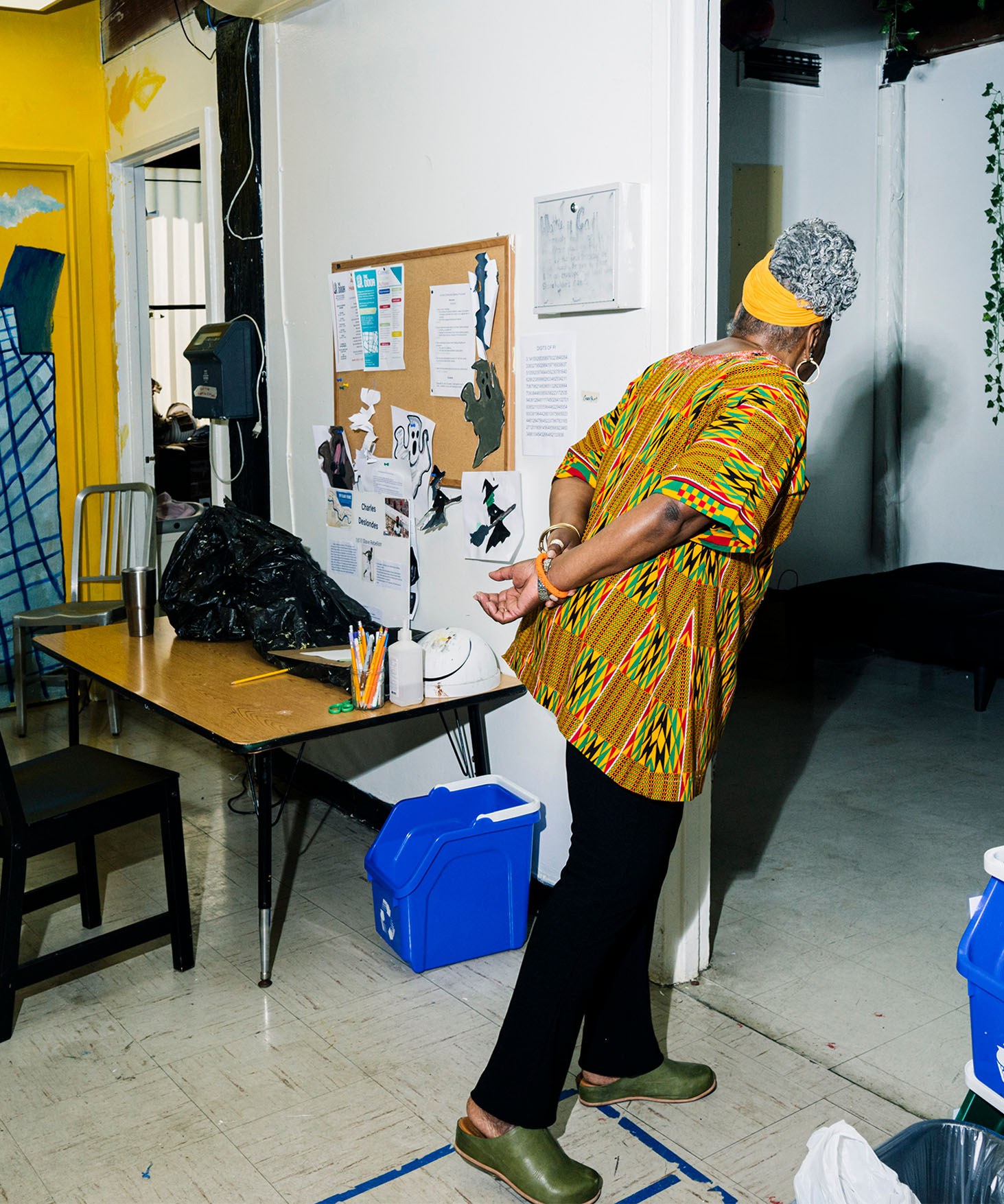 Fela Barclift looking through a doorway in a classroom. Blue recycling bins are visible on both sides of the doorway.
