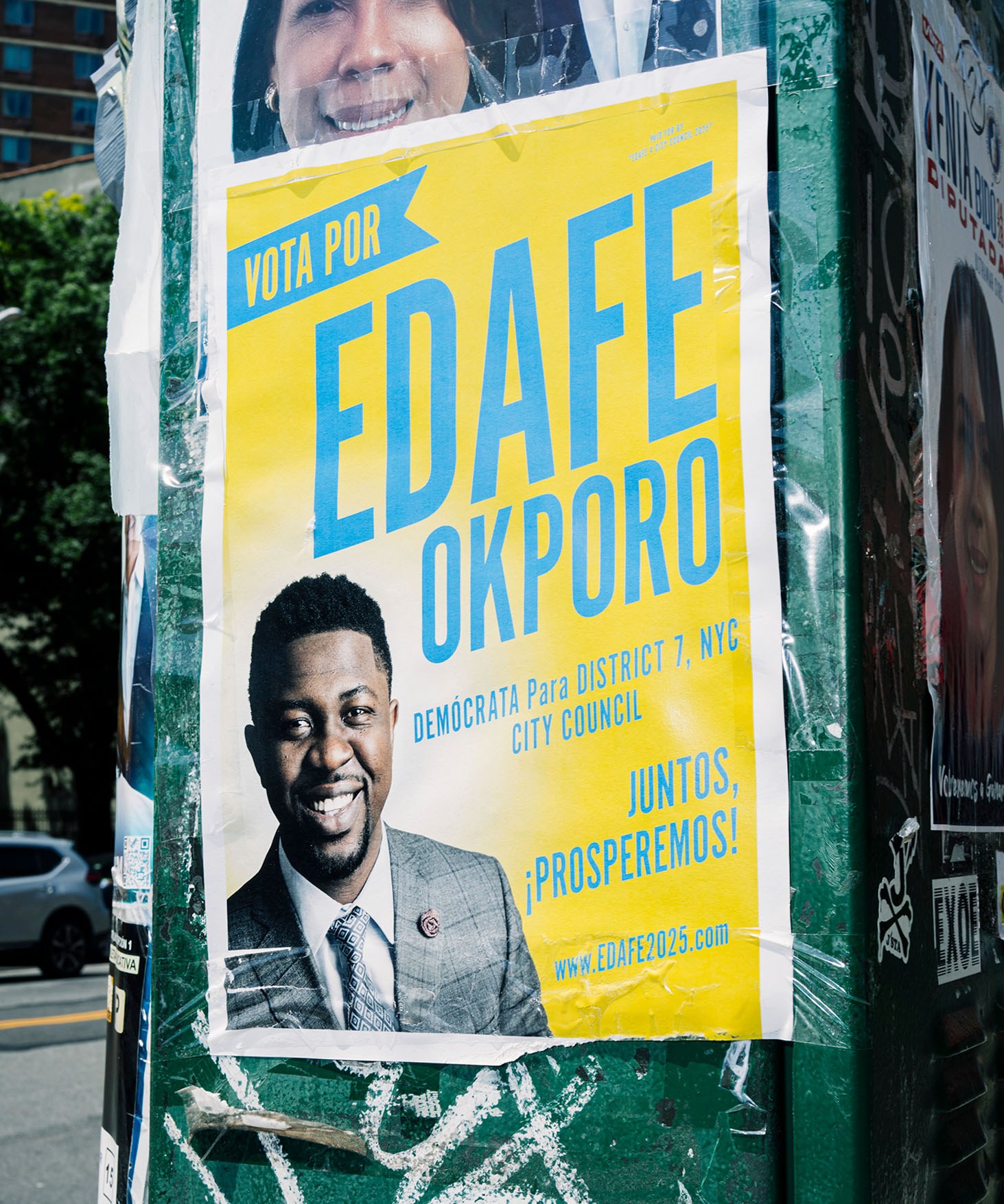A yellow and blue flyer in Spanish that reads, “Vota por Edafe Okporo.” It's mounted to a green traffic box. A New York City street is visible behind.