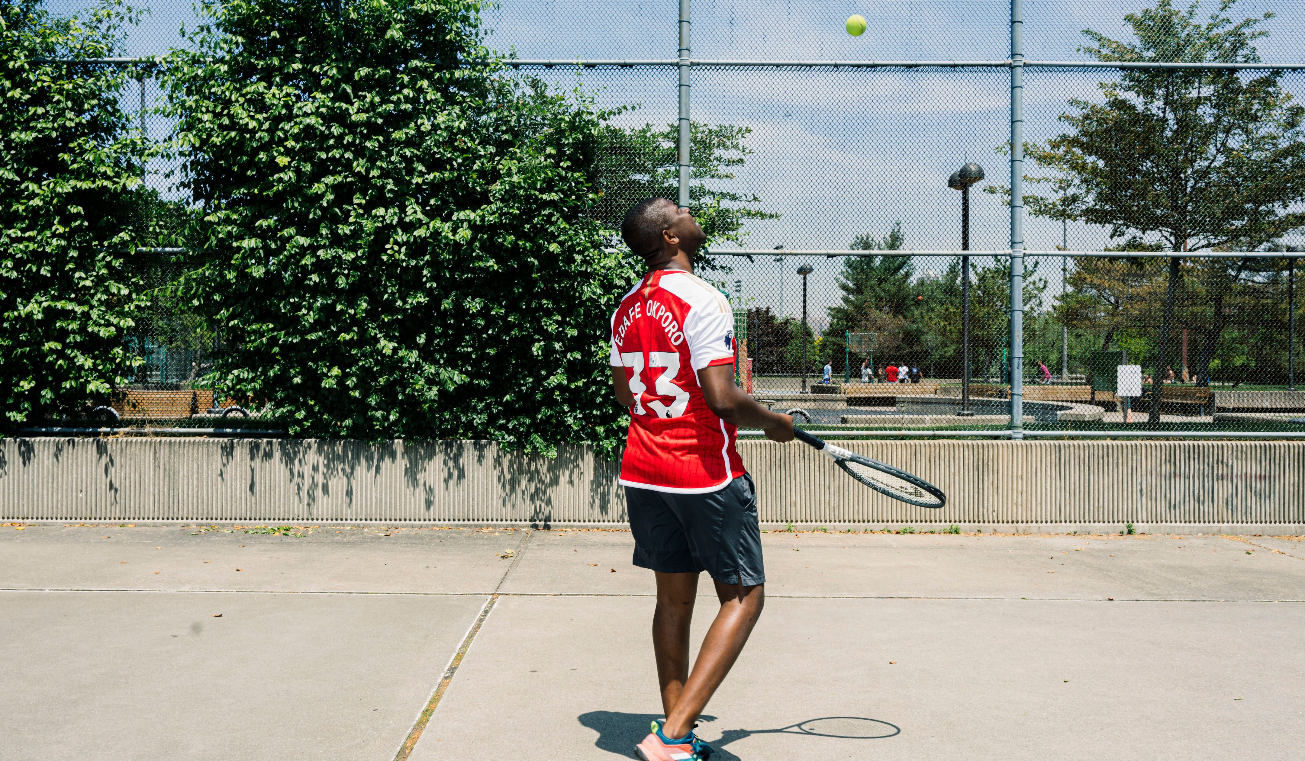 Edafe Okporo holding a tennis racquet, in a playground. He wears a red jersey with his name on it and the number 33.